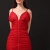 A woman wearing a vibrant red ruched mini dress with spaghetti straps poses confidently against a black background.